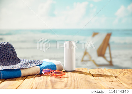 Beachside refreshment. Beer can bottle with hat and towel on beach with beautiful ocean view. 114544349