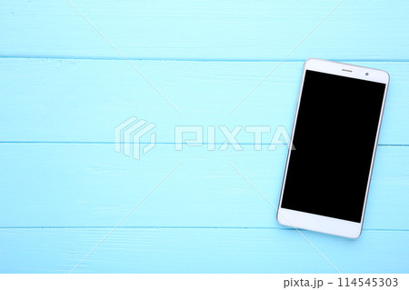 Mobile phone with blank screen on blue wooden background. Smartphone on wood table. Mobile phone with blank screen on blue wooden background. Smartphone on wood table. 114545303