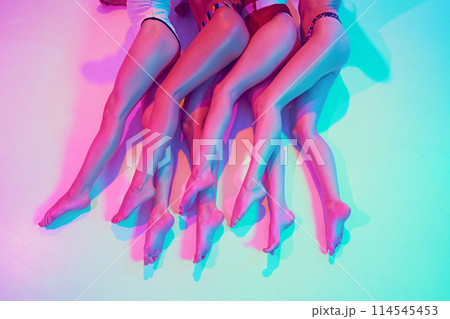 Close-up of four pairs of smooth, slim legs in retro swimwear in neon light against vibrant gradient background. 114545453