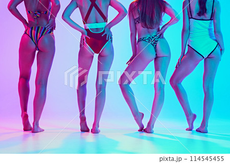 Cropped portrait of slim female models posing in swimwear, showing their legs in neon light against vibrant gradient background. 114545455