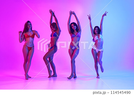 Group of slim, beautiful young women dancing in neon light against vibrant gradient background. Time to relax. Group of slim, beautiful young women dancing in neon light against vibrant gradient background. Time to relax. 114545490