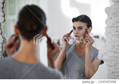 A young woman massages her face with gouache while looking in the mirror. 114545598