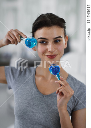 A young woman is massaging her face with blue glass balls while looking in the mirror. 114545615