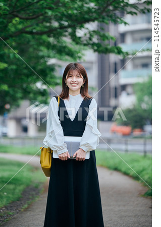 パソコンと手帳を手に持ち歩く若い女性 114545723