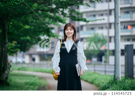 パソコンと手帳を手に持ち歩く若い女性 パソコンと手帳を手に持ち歩く若い女性 114545725