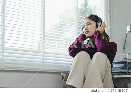 Depressed young woman with headphones sits in a chair and looking away at home. 114546167