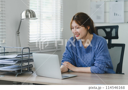 Focused young Asian businesswoman sitting and remote working on laptop computer in a modern home office. Distant workday concept. 114546168