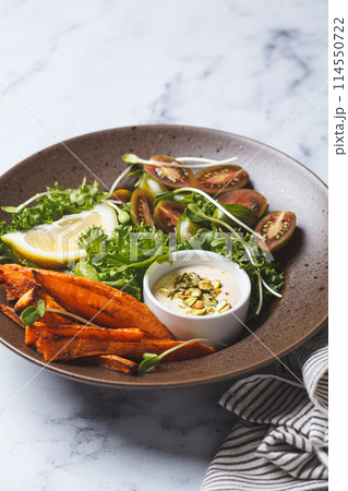 Vegan salad bowl with baked sweet potato, tomatoes, nuts, tahini dressing and sprouts, white background, top view. 114550722