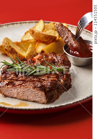Sliced pork steak with baked potato wedges and barbecue sauce 114551505