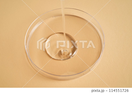 Serum or cosmetic oil flows into a transparent bowl. Serum or cosmetic oil flows into a transparent bowl. 114551726