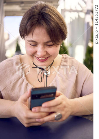 plus size woman in peach fuzz dress chooses a dish in a restaurant via QR code in smartphone, water with lemon and glasses in front of her plus size woman in peach fuzz dress chooses a dish in a restaurant via QR code in smartphone, water with lemon and glasses in front of her 114551772