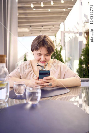plus size woman in peach fuzz dress chooses a dish in a restaurant via QR code in smartphone, water with lemon and glasses in front of her plus size woman in peach fuzz dress chooses a dish in a restaurant via QR code in smartphone, water with lemon and glasses in front of her 114551775