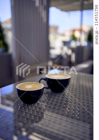 two cups of coffee, latte and cappuccino on a table in a cafe two cups of coffee, latte and cappuccino on a table in a cafe 114551798