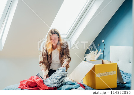 Woman selecting clothes from her wardrobe for recycling, donating to a Charity shop. Decluttering, Sorting clothes, Cleaning Up. Reuse, second hand concept. Conscious consumer, sustainable lifestyle. 114552856