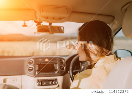 A woman in a yellow shirt is driving a car. She is wearing glasses and has her hands on the steering wheel 114552872