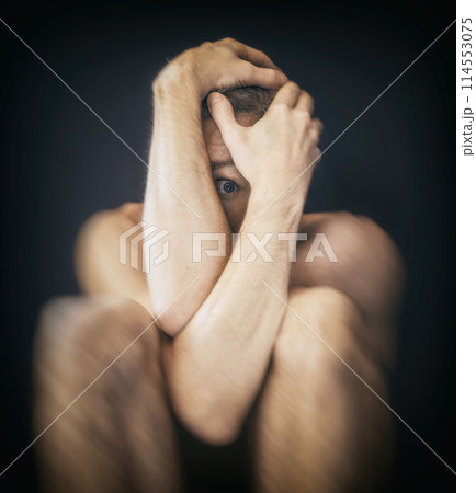 Man sitting in fear covering his face 114553075