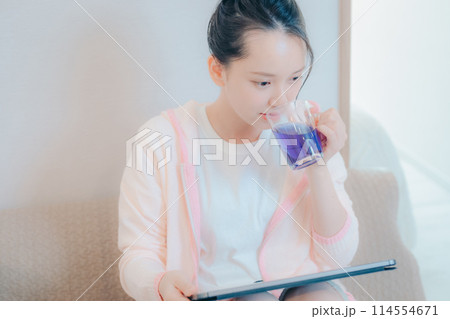 タブレットを見ながらお茶を飲む若い女性 タブレットを見ながらお茶を飲む若い女性 114554671