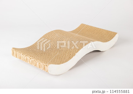 A white background highlights a modern abstract cat scratching post and lounge bed made with corrugated cardboard. cat alertness and playful paw showcase its love for this essential feline furniture. 114555881