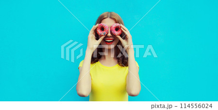 Portrait happy cheerful smiling young woman with sweet donut having fun on blue background Portrait happy cheerful smiling young woman with sweet donut having fun on blue background 114556024