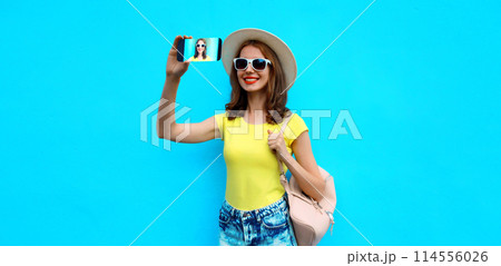 Summer portrait of happy smiling young woman taking selfie with phone wearing hat on blue background Summer portrait of happy smiling young woman taking selfie with phone wearing hat on blue background 114556026