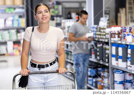Woman shopper stand with trolley filled with goods for repair and coloring in store sales hall. 114556867