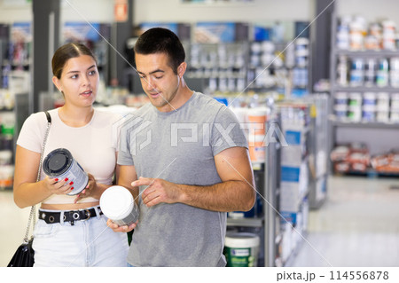 Positive young couple talking and looking for paints in store Positive young couple talking and looking for paints in store 114556878
