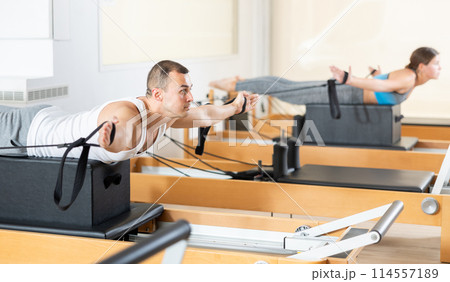 Concentrated man performing exercises with straps on Pilates reformer Concentrated man performing exercises with straps on Pilates reformer 114557189