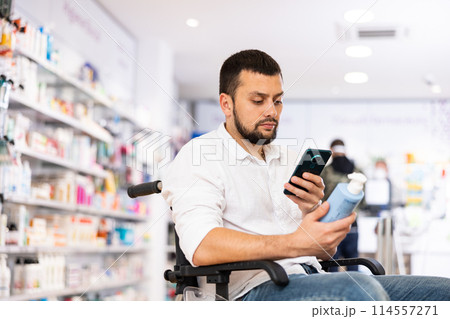 Male customer in wheelchair scans the barcode on medicine bottle with his smartphone Male customer in wheelchair scans the barcode on medicine bottle with his smartphone 114557271