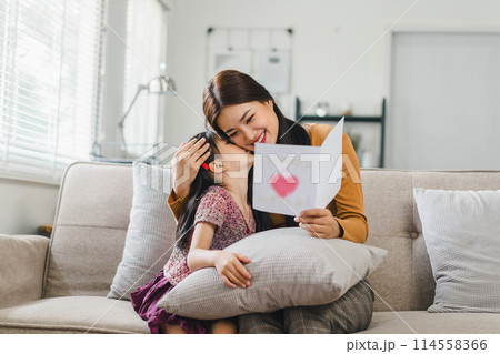 Happy mother's day. Mother receiving a handmade card from her daughter in living room at home. 114558366
