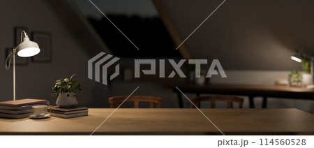 A wooden tabletop in a modern dark attic room at night with dim light from table lamps. 114560528