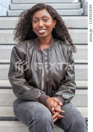 Smiling African American Woman Sitting on Steps in Casual Fashion 114561694