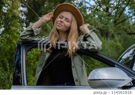 Blonde woman in hat staying next to car door. Young tourist explore local travel making candid real moments. True emotions expressions of getting away and refresh relax 114561918