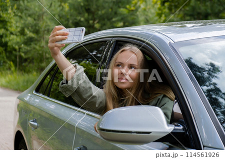 Blonde woman stoped car on road to take a selfie photo. Young tourist explore local travel making candid real moments. True emotions expressions of getting away and refresh on open air Blonde woman stoped car on road to take a selfie photo. Young tourist explore local travel making candid real moments. True emotions expressions of getting away and refresh on open air 114561926