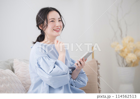 綺麗なリビングでスマホを持って考える若い女性　思い付く笑顔 114562513
