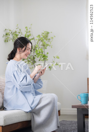 綺麗なリビングでスマホを持って考える若い女性　画面を見て笑顔で何かを見つける　縦長 114562523