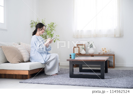 綺麗なリビングでスマホを持って考える若い女性　画面を見て笑顔で何かを見つける広角の全身 114562524