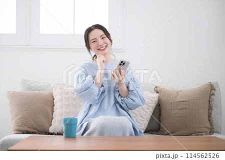 綺麗なリビングでスマホを持って考える若い女性 笑顔で何かを見つける 正面 カメラ目線で首を傾げる 綺麗なリビングでスマホを持って考える若い女性 笑顔で何かを見つける 正面 カメラ目線で首を傾げる 114562526
