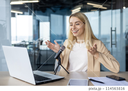 A cheerful blonde woman is hosting a podcast, speaking engagingly into a microphone, using a laptop in a contemporary office space with daylight. A cheerful blonde woman is hosting a podcast, speaking engagingly into a microphone, using a laptop in a contemporary office space with daylight. 114563816