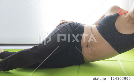 産後の妊娠線が残るお腹とヨガマットの上で腰をひねる女性 産後の妊娠線が残るお腹とヨガマットの上で腰をひねる女性 114563999
