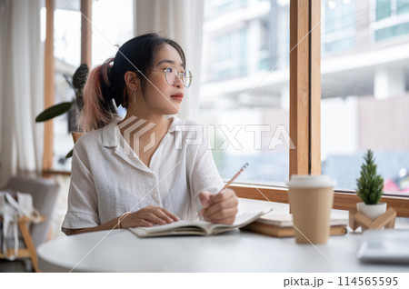 A college student is pondering thinking something while doing her homework in a coffee shop. A college student is pondering thinking something while doing her homework in a coffee shop. 114565595