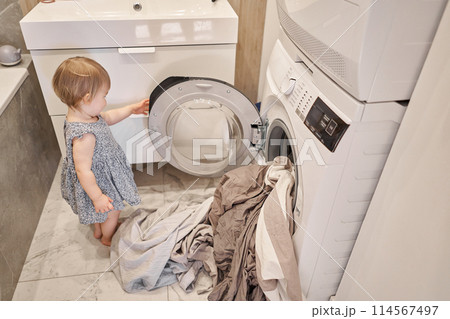 changing of bed linen while House cleaning. Happy baby girl one and a half, helper are having fun and smiling while in a bright apartment. Helps parents change bed linen and do laundry in the washing changing of bed linen while House cleaning. Happy baby girl one and a half, helper are having fun and smiling while in a bright apartment. Helps parents change bed linen and do laundry in the washing 114567497