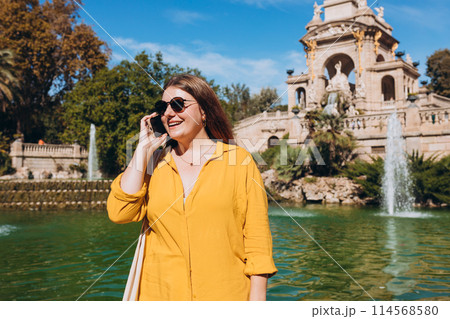 Beautiful stylish woman in trendy wear spending time on street using smartphone. Happy girl talking on the mobile phone near Ciutadella Park in Barcelona. Traveling Europe Beautiful stylish woman in trendy wear spending time on street using smartphone. Happy girl talking on the mobile phone near Ciutadella Park in Barcelona. Traveling Europe 114568580