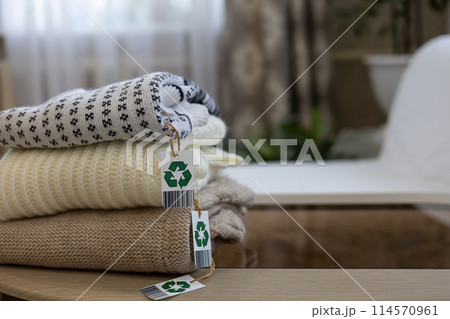 Copy space. Clothes with a recycling label are stacked on a table in the living room. Sorting old clothes for recycling or sale. Clothes were folded and prepared for recycling, sale and donation. 114570961