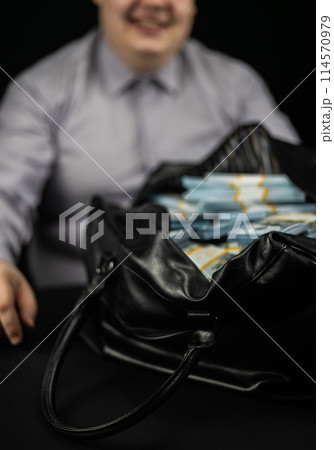 Happy man smiling with a bag full of money on a black background. Happy man rejoices over a big win, smiling over a bag with money. Concept of winning, luck, jackpot. Happy man smiling with a bag full of money on a black background. Happy man rejoices over a big win, smiling over a bag with money. Concept of winning, luck, jackpot. 114570979