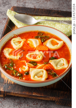 Tomato tortellini soup with vegetables and spinach close-up in a plate. Vertical 114571034