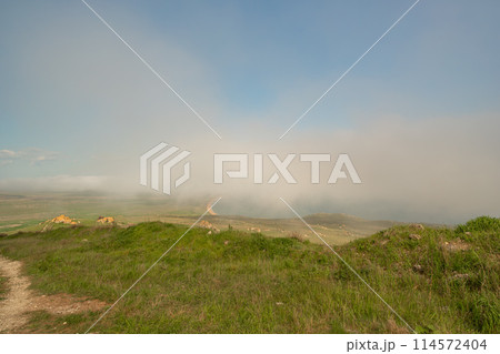 A foggy day with a cloudy sky and a grassy hill. The sky is blue and the clouds are white. 114572404