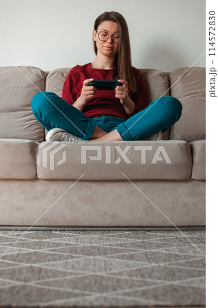 Woman using mobile phone, holding in hands sitting on sofa Woman using mobile phone, holding in hands sitting on sofa 114572830