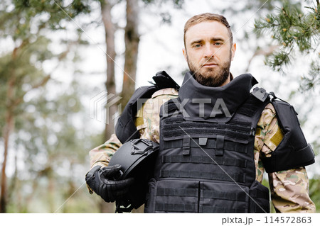 Young soldier in uniforms and tactical vest works in the forest and prepares for action at a temporary forest base. A man does in the work of demining the territory 114572863