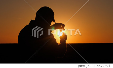 Silhouette of a farmer examining seedlings in the field. Back view Silhouette of a farmer examining seedlings in the field. Back view 114572891