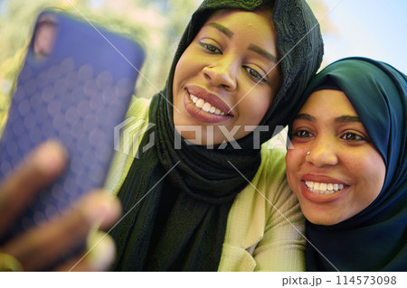 Middle Eastern Muslim Women Capturing Selfies in Serene Surroundings 114573098